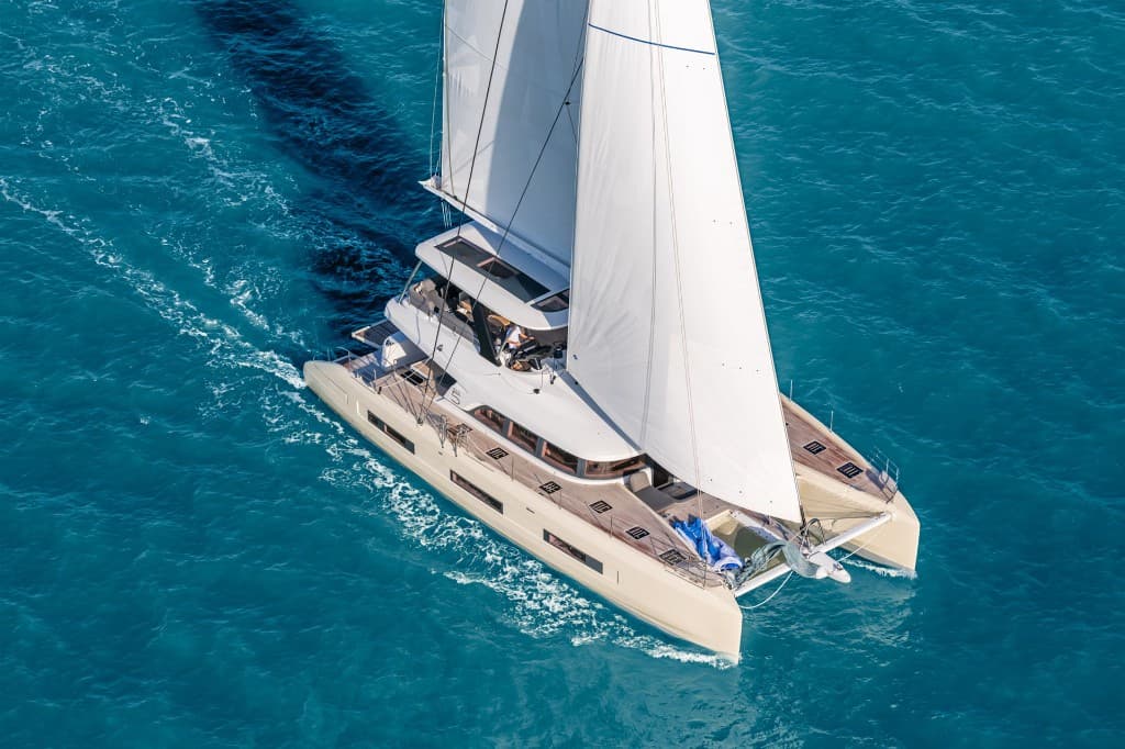 Aerial view of a luxury white sailing catamaran with large sails on clear turquoise water