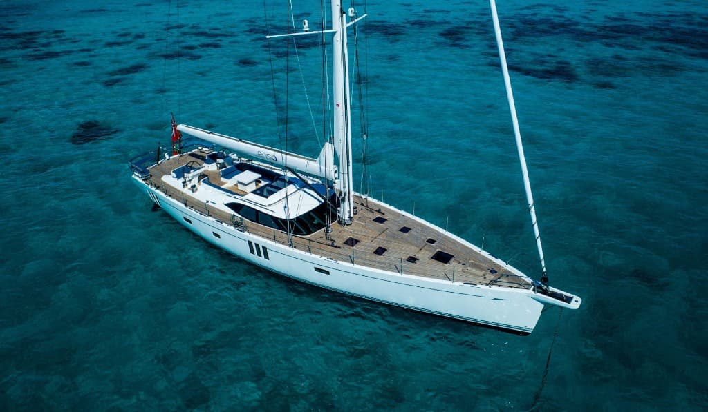Aerial view of a luxury white sailing yacht anchored in clear turquoise water, wooden deck and navy cockpit seating